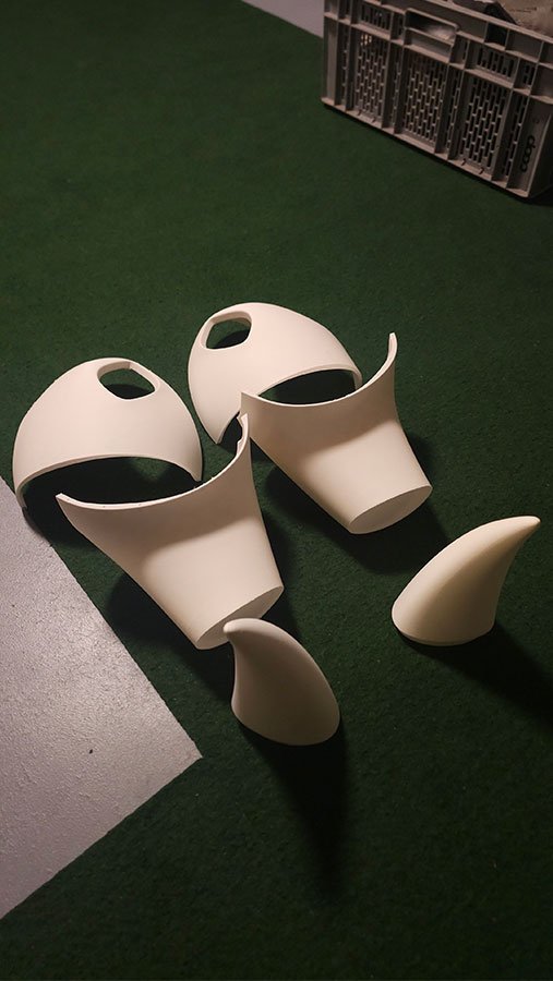 Deux masques blancs imprimés en 3D, avec de grandes ouvertures noires, sur un fond vert