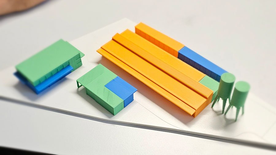 Éléments d'une maquette architecturale en orange, vert et bleu, disposés avant assemblage