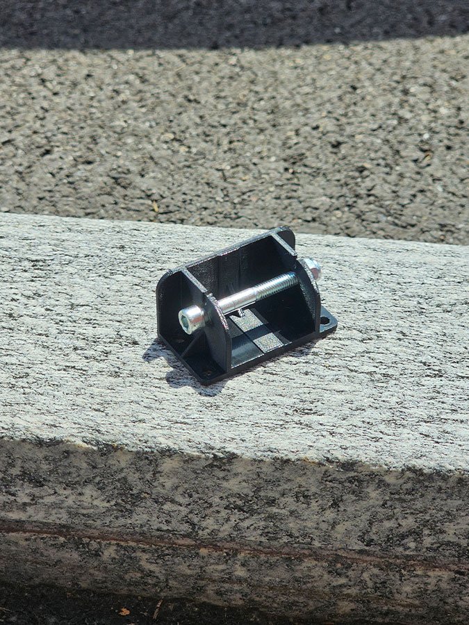 Pièce de fixation noire avec une vis métallique, posée sur une marche en pierre