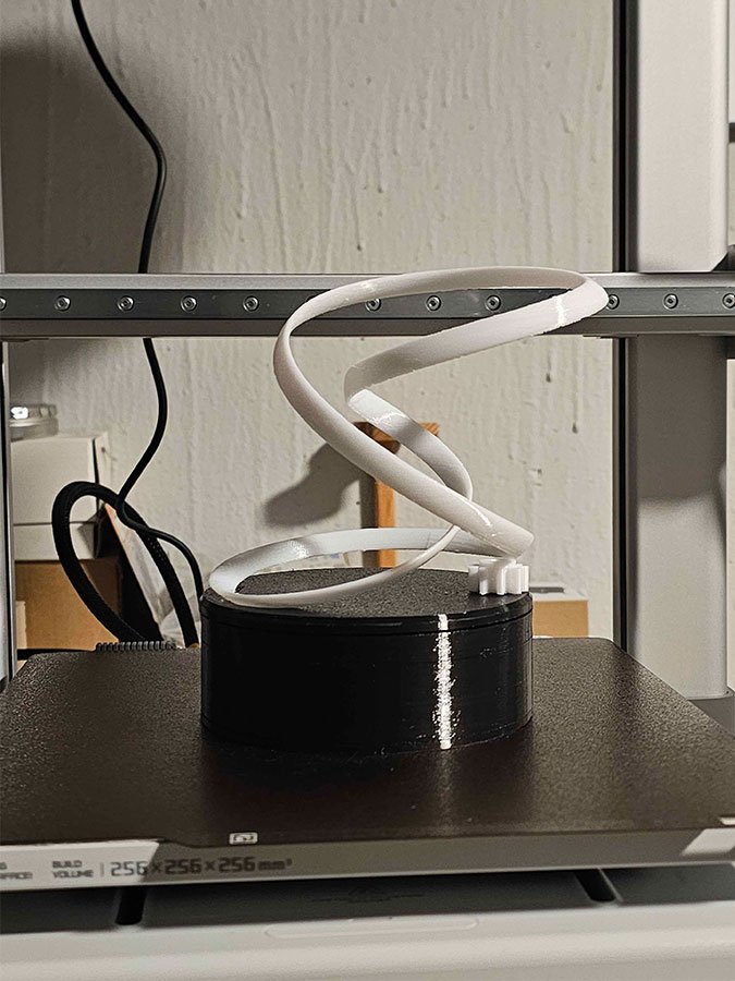 Spirale blanche imprimée en 3D sur un socle noir, posée sur le plateau de l'imprimante